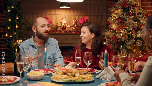 Festive couple celebrating Christmas at evening dinner table with close family members. Positive people sitting in living room to celebrate authentic traditional winter holiday with loved ones.