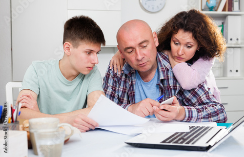 Parents with teenager son reading and writing some documents at home table ..