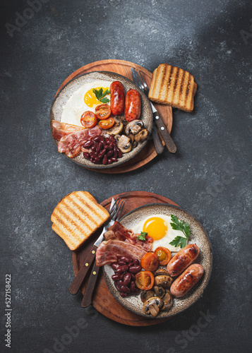 Traditional full English breakfast with fried eggs, sausages, beans, mushrooms, grilled tomatoes, bacon and toasts on gray plates. photo