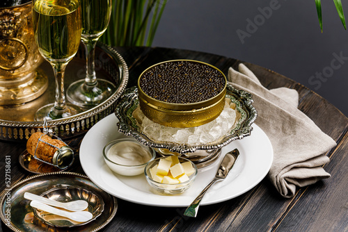 Black caviar on ice in silver bowl and Champagne close-up photo