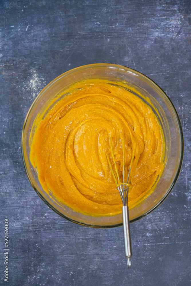 Pumpkin muffin batter with cornmeal in a mixing bowl and a hand whisk inside it. Pumpkin muffin batter with cornmeal in a mixing bowl and a hand whisk inside it.