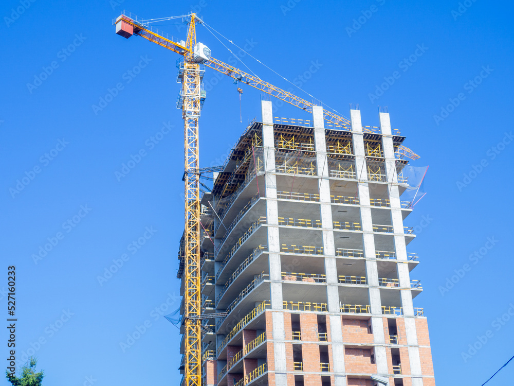 Fototapeta premium Crane and frame of a high concrete house. Construction works. Concrete construction. Skeleton at home