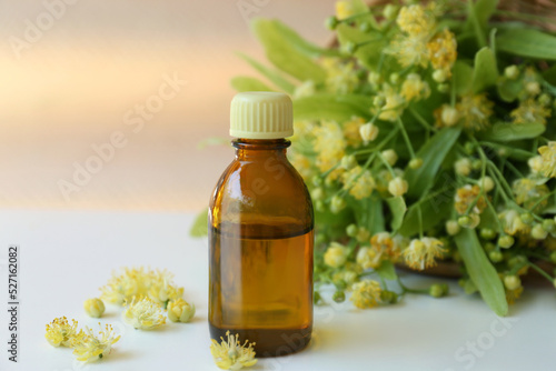Fototapeta Naklejka Na Ścianę i Meble -  Bottle of essential oil and linden blossoms on white table