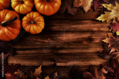 Pumpkins with fall leaves over wooden background. Top view.