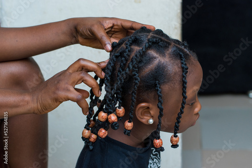 Hands of an african hair stylist or mother making braided hairstyle on the head of a little girl child at a saloon