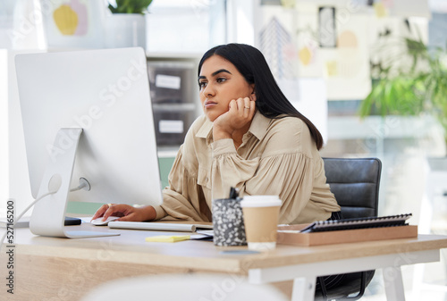 A bored, lazy and tired employee working on a computer in the office leaning on her desk. An overworked business woman is annoyed and frustrated by her job sitting at her table feeling burnout