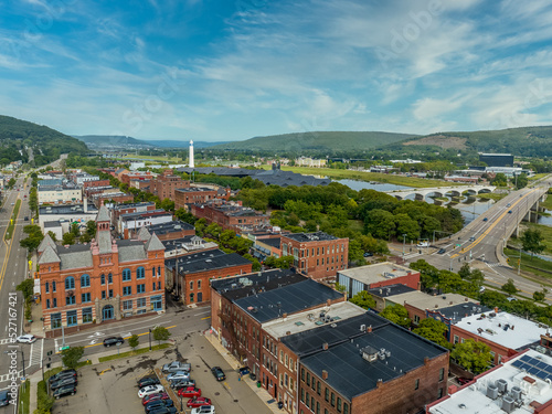 Aerial view of Corning Steuben County, New York downtown, Market Street, glass factory, chemung river, centerway walking bridge, little joe tower, parking lot with cloudy blue sky photo