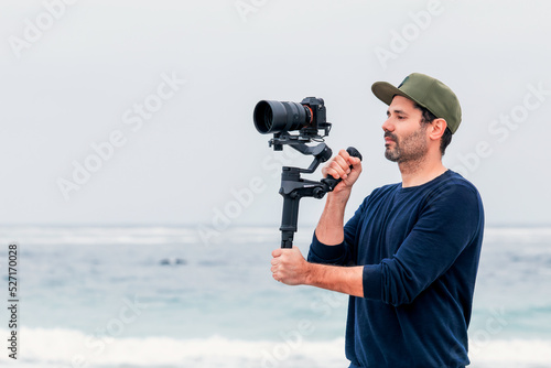 mature male on the beach holding a camera on a gimbal or stabilizer filming