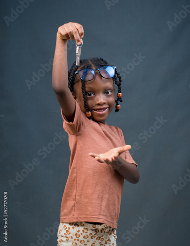 A cute and happy African girl child from Nigeria with eye glasses, dancing and holding house keys in her hand