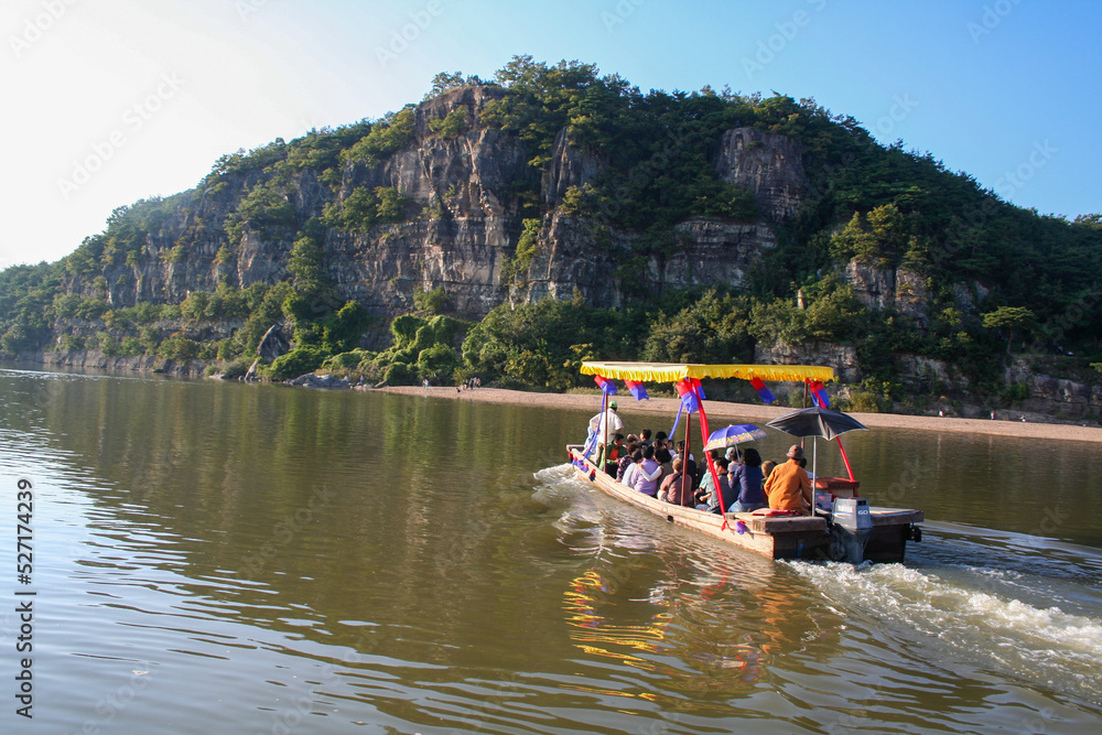 Naklejka premium A boat crosses a river approaching a small sandy beach at the base of a cliffside.