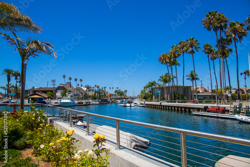 Fototapeta Naklejka Na Ścianę i Meble -  a gorgeous summer landscape at Naples Canals with blue ocean water surrounded by colorful flowers, lush green palm trees and plants and boats docked along the banks with a clear blue sky in Long Beach
