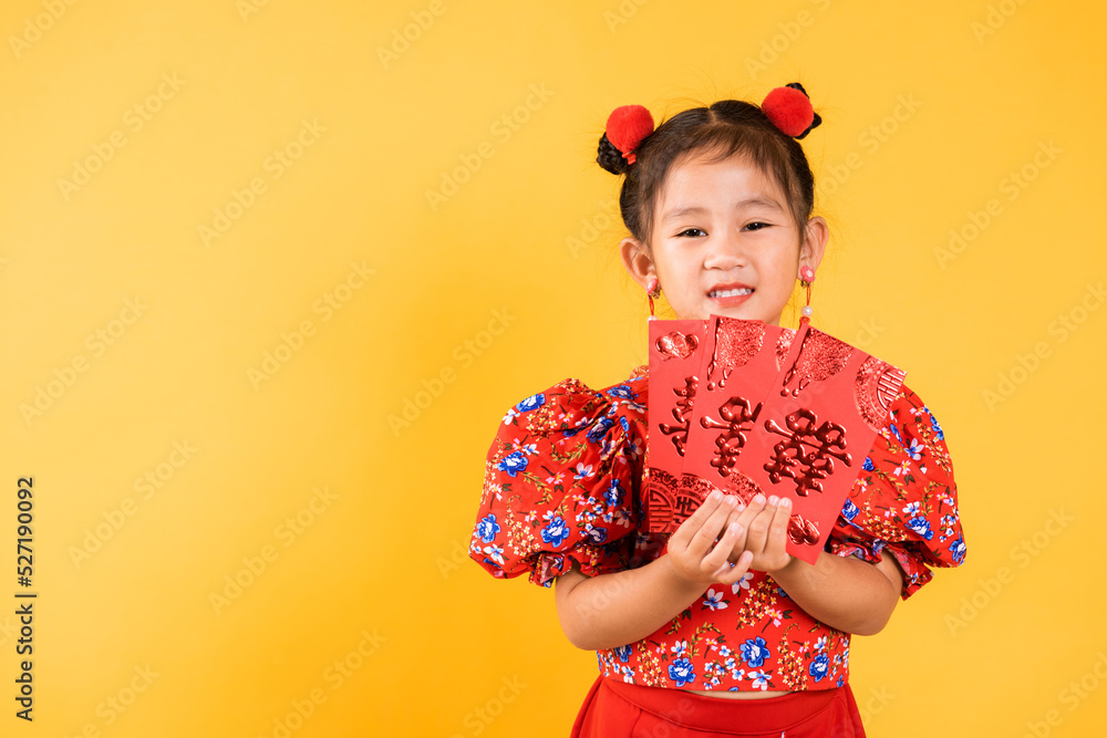 Chinese New Year. Happy Asian Chinese little girl smile wear red cheongsam qipao hold angpao red packet monetary gift, Portrait child in traditional dress, studio short isolated on yellow background Chinese New Year. Happy Asian Chinese little girl smile wear red cheongsam qipao hold angpao red packet monetary gift, Portrait child in traditional dress, studio short isolated on yellow background