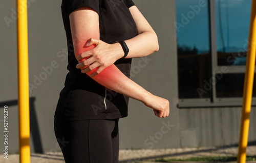 Woman doing sport and suffering from elbow pain. Female holding painful arm with red point during training outdoors. Injury consequences © valiantsin