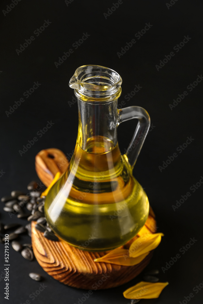 Cutting board with jug of oil and sunflower seeds on black background