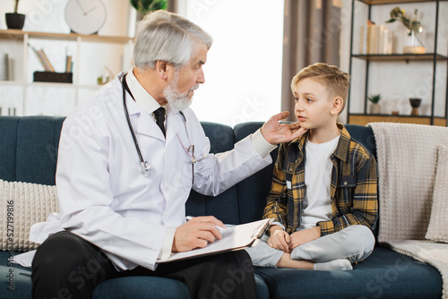 Mature doctor groping checking pain and swelling in the neck sore throat and cough thyroid nodule inflammation of the lymph nodes tonsillitis of sick male patient boy during home visit photo