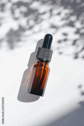 Amber bottle with cannabis oil used for medical purposes. White background with daylight and flowers shadows. Soothing cbd oil. Alternative Medicine