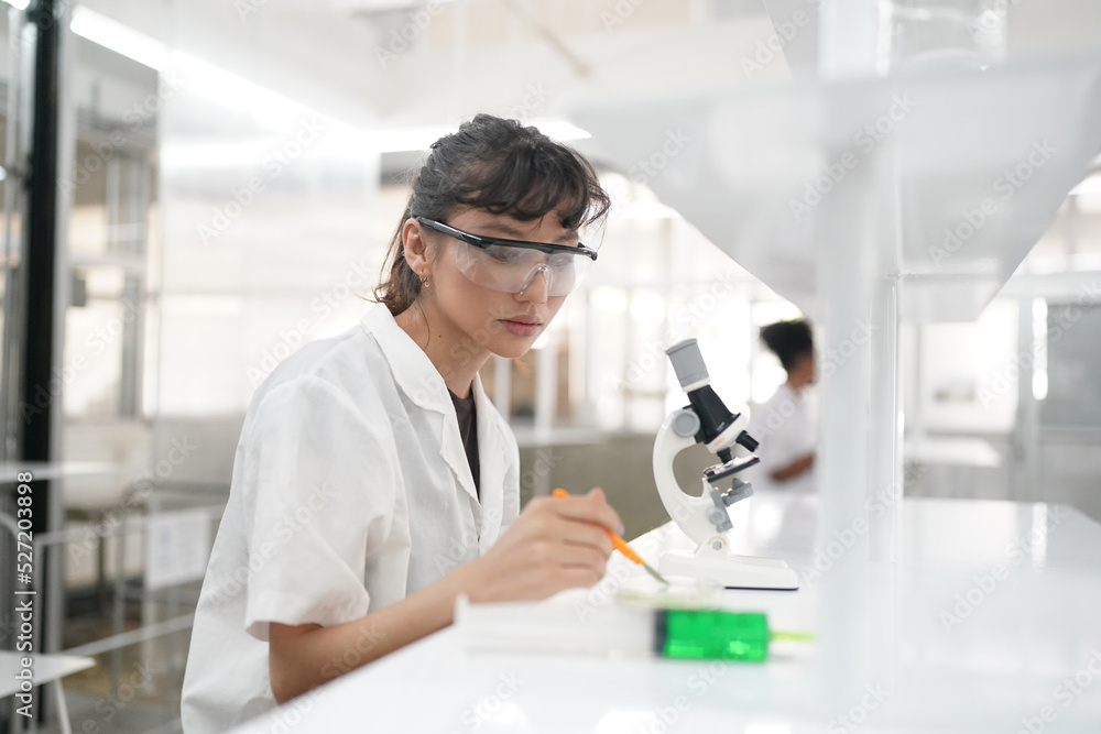 Young scientist in white lab coat working with binocular microscope in the material science lab Young scientist in white lab coat working with binocular microscope in the material science lab