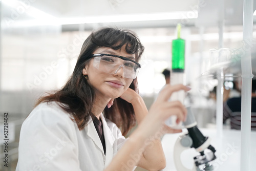 Young scientist in white lab coat working with binocular microscope in the material science lab