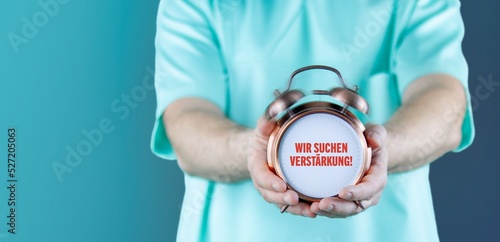 Wir suchen Verstärkung! (Arztpraxis). Doktor zeigt Uhr/Wecker mit Text. Hintergrund blau photo