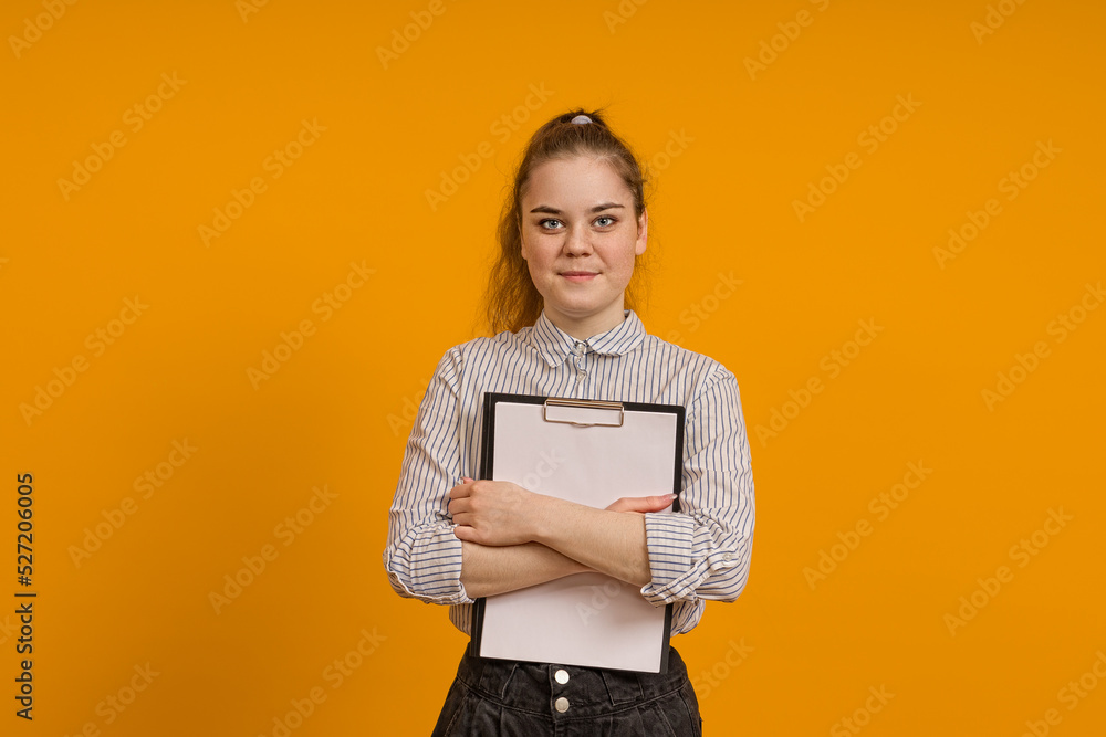 a teenager girl hugged a tablet for papers and stands on a yellow background a teenager girl hugged a tablet for papers and stands on a yellow background