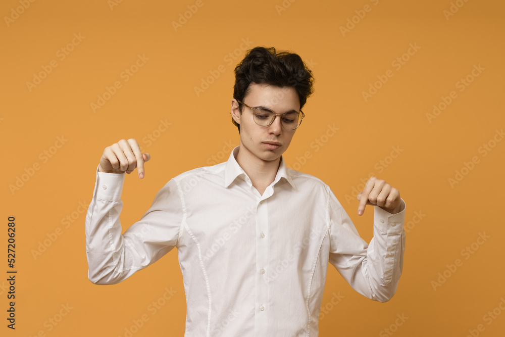 student guy in a white shirt looks down and points with fingers, colored background student guy in a white shirt looks down and points with fingers, colored background