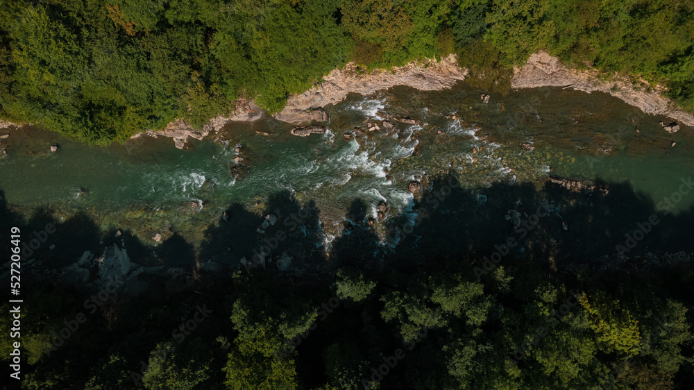 Mountain emerald river with stone coast and forest, strong stream with twists of crystal clear mountain river. Aerial drone top down view at summer sunny day