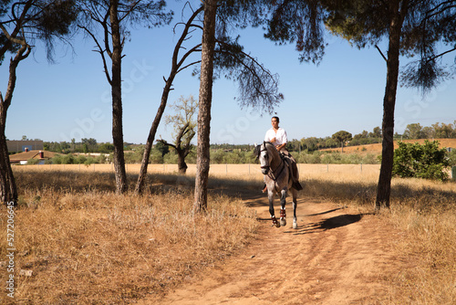 Young and beautiful Spanish woman on a Thrush horse galloping through the countryside in Spain. The woman is wearing a horse riding uniform. Thoroughbred and equine concept.