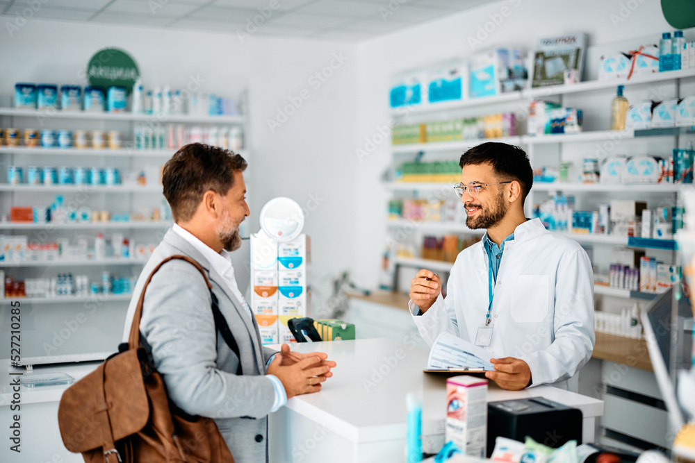 Happy pharmacist advising male customer in pharmacy.