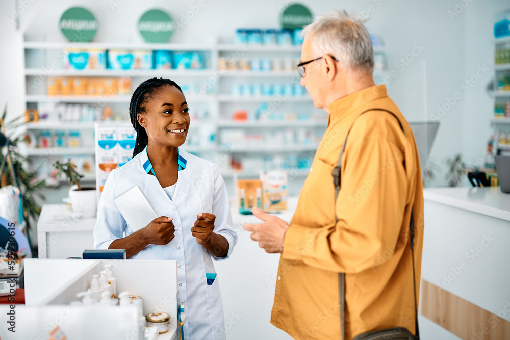 Obraz premium Happy African American pharmacist talks to senior man in pharmacy.