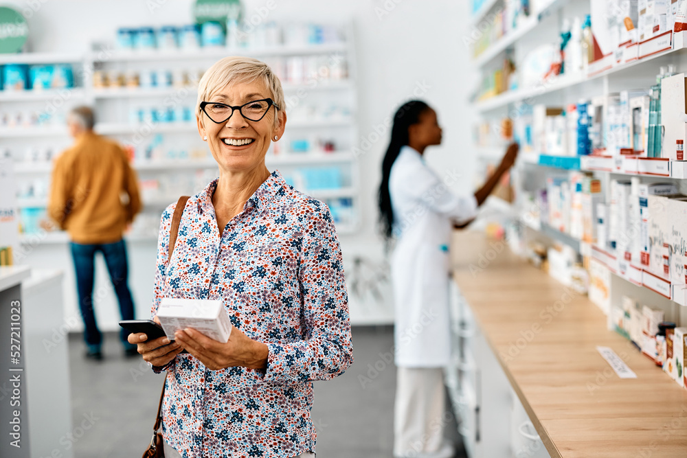 Happy senior woman buying medicine in pharmacy and looking at camera.
