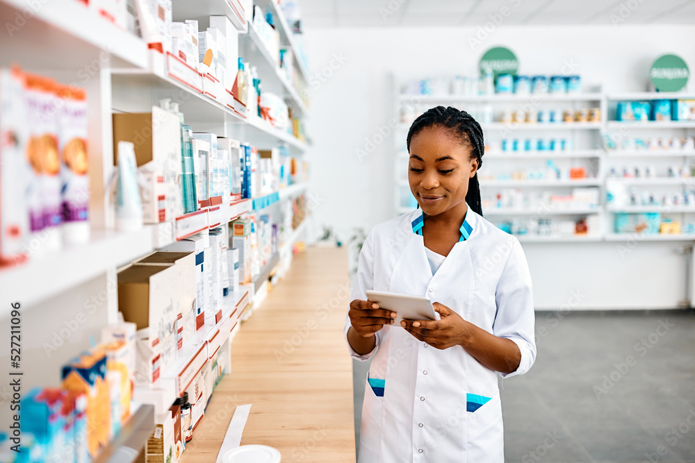 Black female pharmacist working on digital tablet in pharmacy.