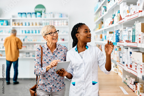 Young black pharmacist assists senior woman in buying medicine in pharmacy.