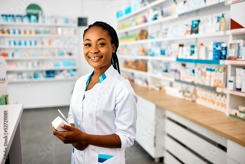 Happy African American pharmacist working in drugstore and looking at camera.