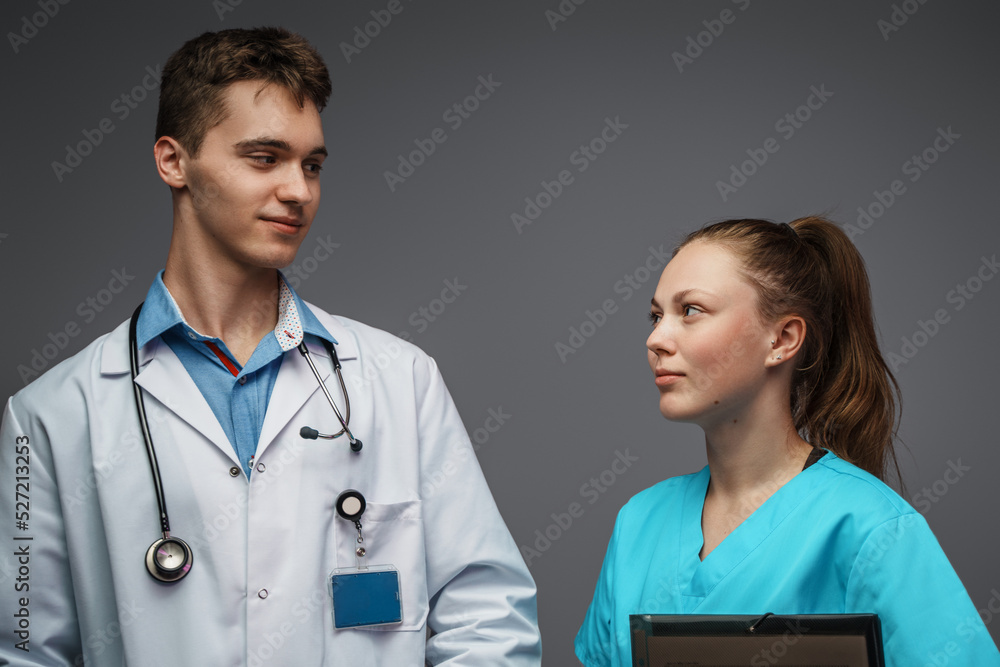 Photo of nurse with folder and doctor dressed in white labcoat looking each other. Photo of nurse with folder and doctor dressed in white labcoat looking each other.