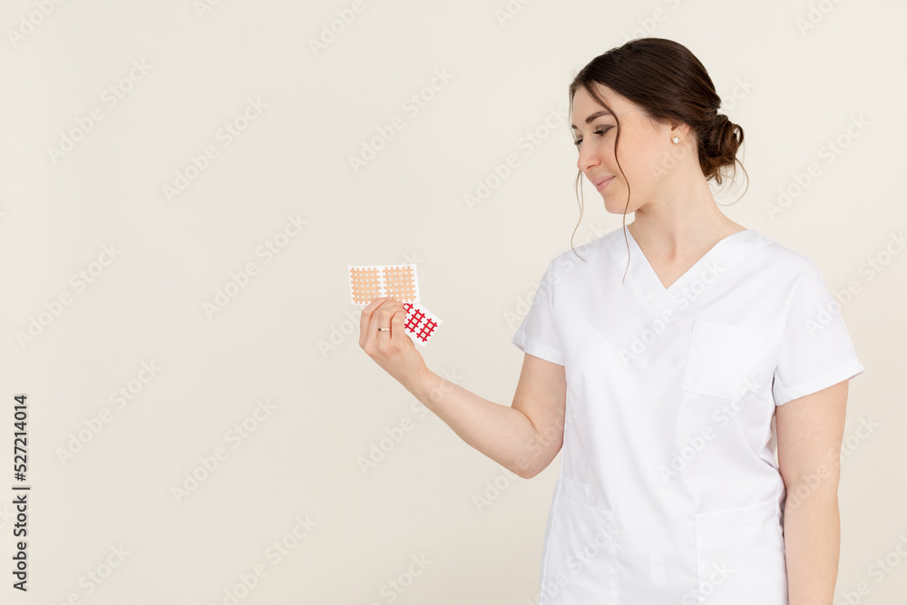 Side view of young attractive masseuse therapist woman wearing white uniform, holding and looking at beige cross tapes. Side view of young attractive masseuse therapist woman wearing white uniform, holding and looking at beige cross tapes.