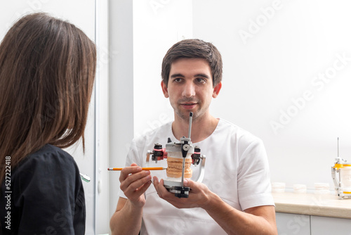 Dentist holding dental articulator with dental gypsum prosthesis model showing it to a patient photo