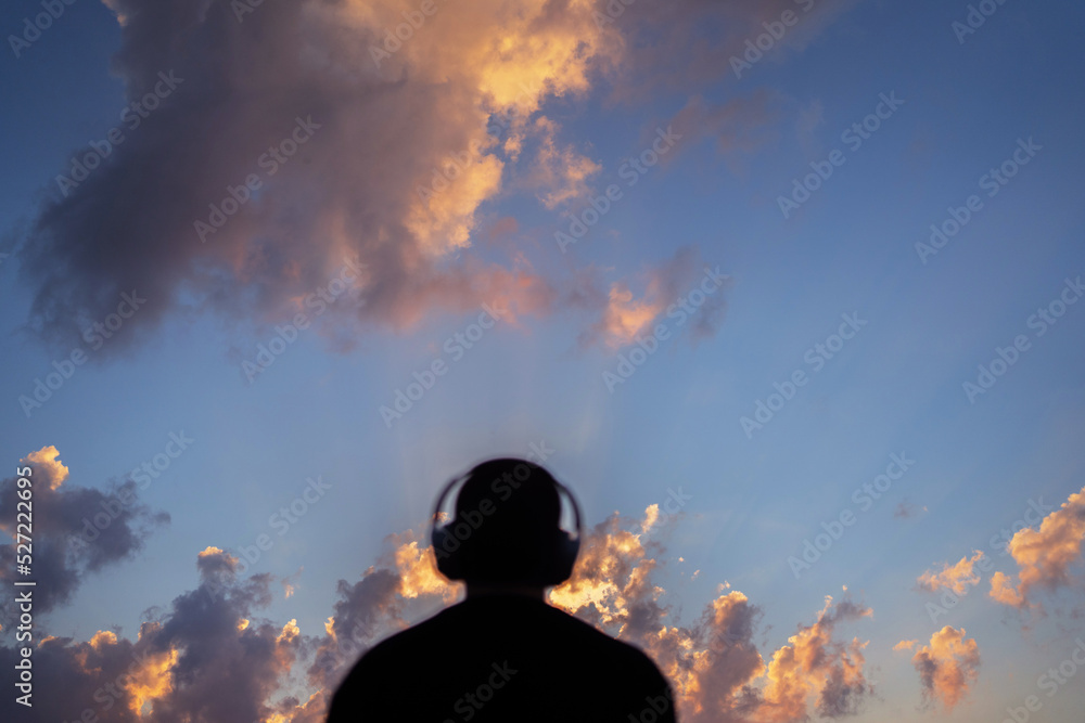 A man relax listens to calm music looks at the sunset with headphones harmony with nature