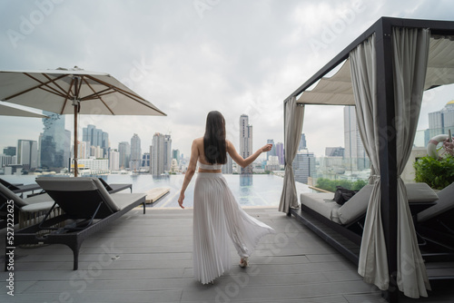 Photography Young woman in a white dress is standing on the pool on a tall building behind the city view in the heart of Bangkok