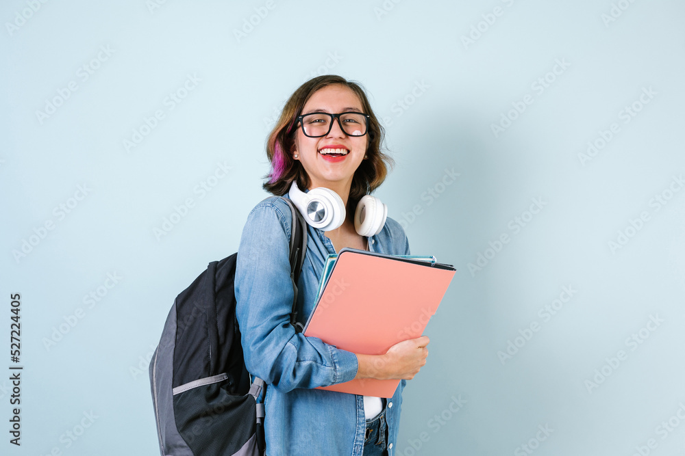 Obraz premium Young Hispanic student teen girl woman holding books with glasses over isolated blue background in Latin America