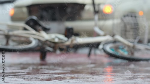 Blurred out of focus bicycle falling down on the road in front of a car after involved in traffic accident on a raining day