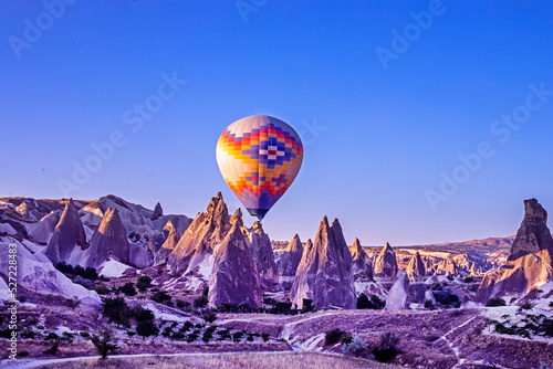 hot air balloon in the blue sky in front of bizarre mountain silhouettes in the Cappadocia valley in the early morning.