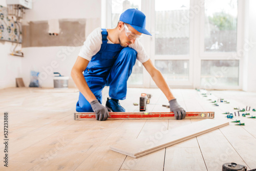 Adult repairman in a special uniform laying tiles with tile leveling system on the floor in a new house