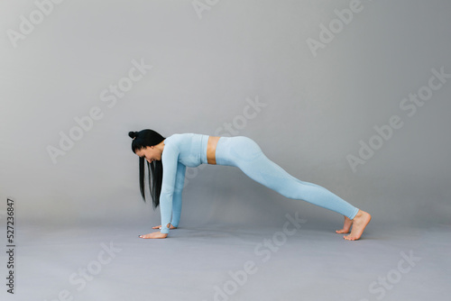 athletic fitness woman in blue sportswear, training in isolation on a gray background of a studio portrait. Sports exercises are the concept of a healthy lifestyle. Performing plank exercises