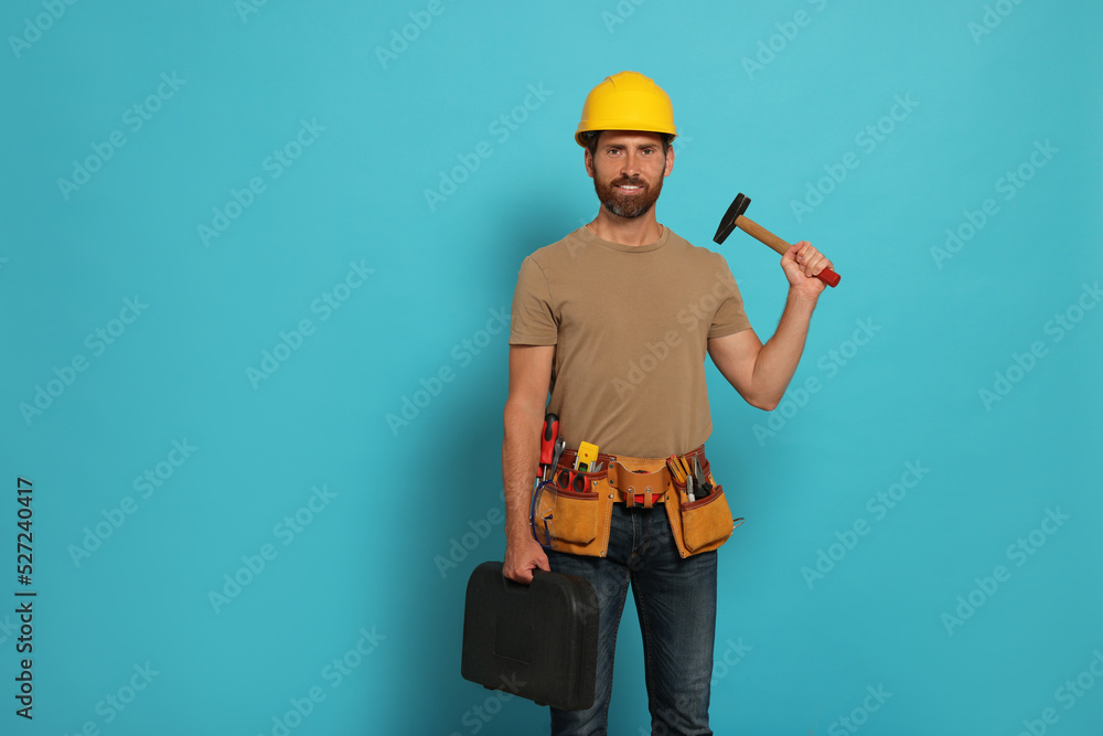 Professional builder in hard hat with hammer and tool belt on light blue background Professional builder in hard hat with hammer and tool belt on light blue background