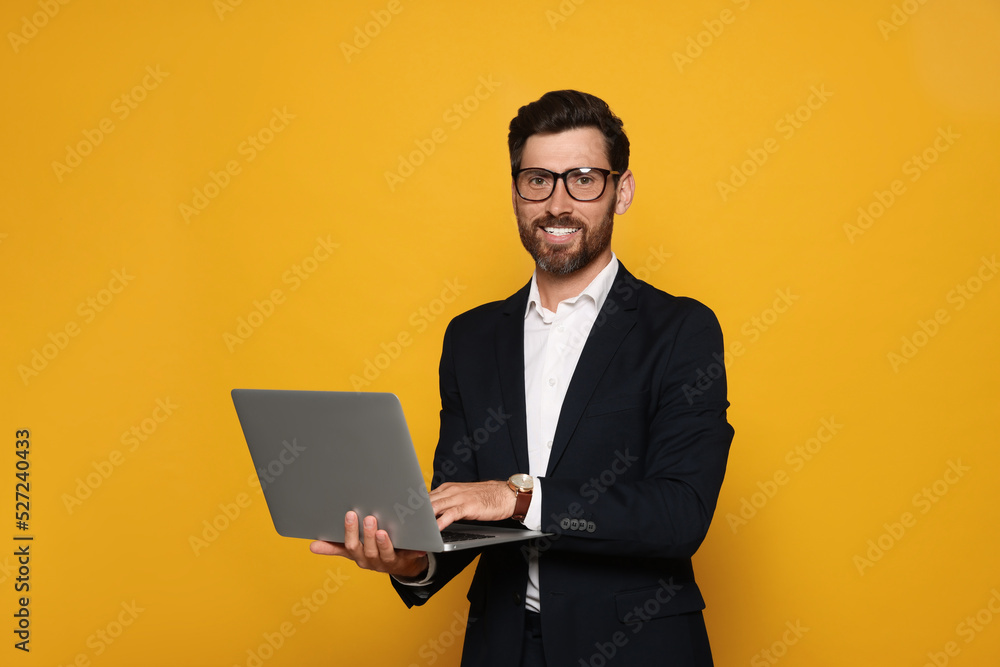 Portrait of smiling bearded man with glasses and laptop on orange background