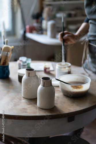 Crop photo of skilled master leaving clay vases to dry out on table after baking and handmade shaping in studio. Craftsworker hands put necessary appliances for painting vase on table in special shop