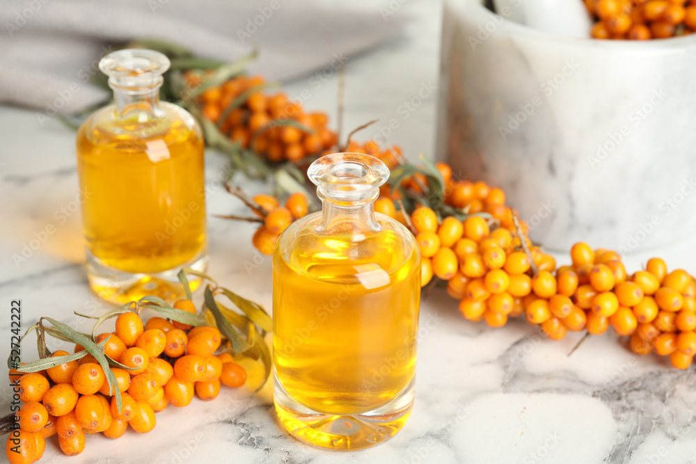 Natural sea buckthorn oil and fresh berries on white marble table Natural sea buckthorn oil and fresh berries on white marble table