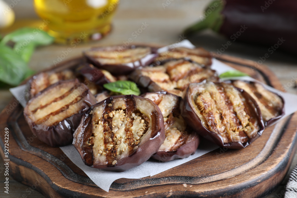 Delicious grilled eggplant slices served on wooden board, closeup