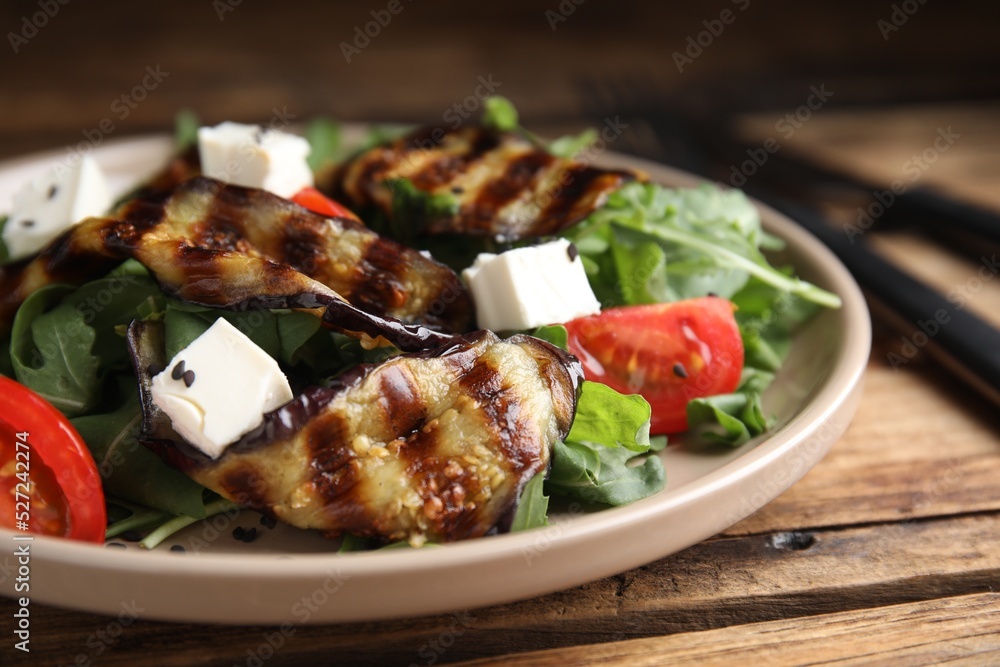 Delicious salad with roasted eggplant, feta cheese and arugula served on wooden table, closeup