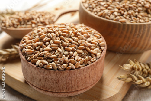 Wheat grains in bowls on wooden board, closeup